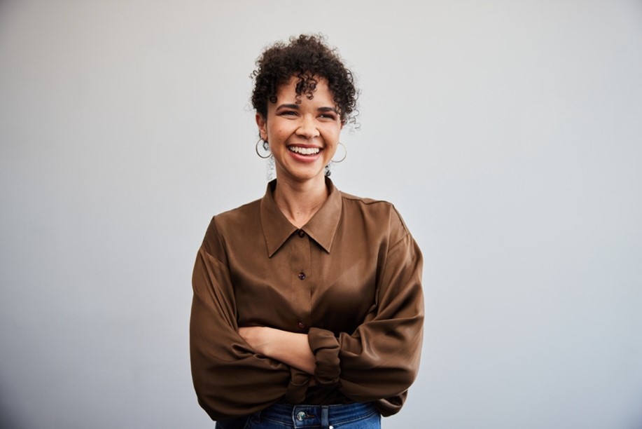 A person with curly hair wearing a brown shirt and jeans